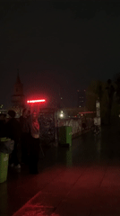 Nighttime gathering features red light art installation near tower