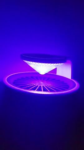 A purple LED light emits from a device that is positioned in a dark environment. The device has a conical, clear light-diffusing attachment that is illuminated by white LEDs from above. Below the conical attachment is a circular grate, which is also illuminated by the purple LED light. The device appears to be a bug zapper.