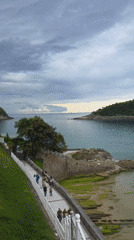 Pedestrians stroll coastal walkway in San Sebastián on cloudy afternoon