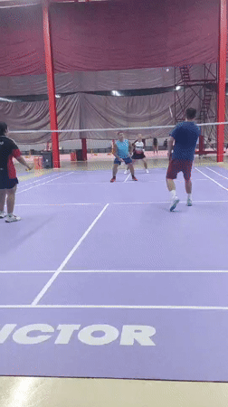 Badminton doubles match captured on indoor purple court