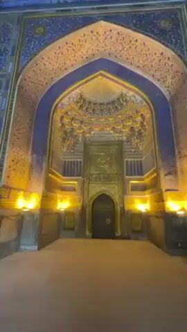 The video shows an ornately decorated interior space with intricate mosaic tile work in blue, gold, and white. The camera pans up from a large arched doorway to reveal a domed ceiling covered in complex geometric patterns. The room is illuminated by warm artificial light. A person speaking can be heard in the background.