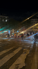 Cyclists navigate wet Paris intersection at night