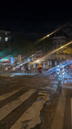 Cyclists navigate wet Paris intersection at night