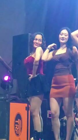 The video shows a group of women dancing on a stage. There are large speakers and lighting equipment visible in the background, suggesting a performance or event. The women are dressed in revealing clothing and appear to be engaged in a lively dance routine. The overall atmosphere seems to be energetic and festive.