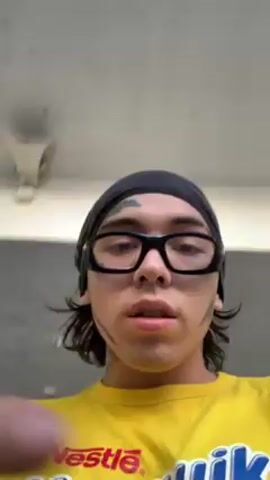 A young person with a black head covering, black glasses, and a yellow t-shirt points their finger toward the camera. They then spin the camera upward to reveal an elevated train track with a train passing overhead. The camera spins back down to face the person.