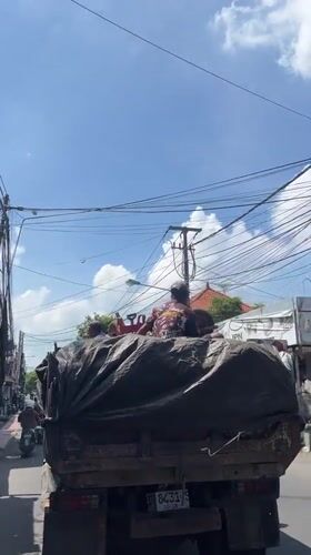Three passengers ride in truck bed through Ubud streets