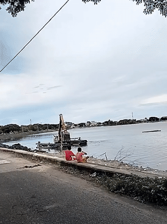 Children watch dredging operations in Lhokseumawe waterway