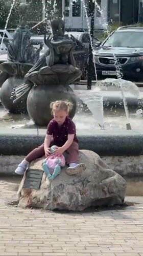 Child plays near fountain while woman takes selfie in Dmitrov