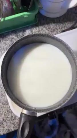 Here's a description of the video:

The video shows a person preparing food in a kitchen.  A pot containing a white liquid, possibly milk, sits on the counter next to a container with a white powder inside. The person moves the container of powder slightly.  Other items visible in the scene include cleaning supplies, and other containers.  The countertops are a speckled gray.