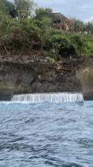 Boat navigates dramatic Nusa Penida coastline under overcast skies