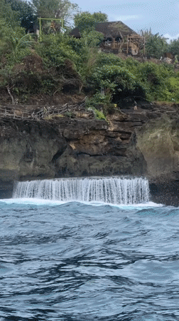 Boat navigates dramatic Nusa Penida coastline under overcast skies