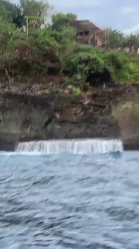Boat navigates dramatic Nusa Penida coastline under overcast skies