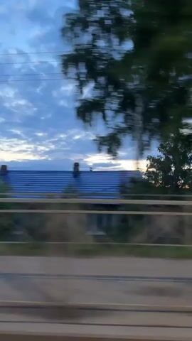 The video shows a blurry, fast-moving view of houses and trees passing by. The sky is partly cloudy with hints of orange and yellow from a sunset. Power lines are visible in the upper portion of the frame. The motion suggests the footage is being filmed from a moving vehicle.