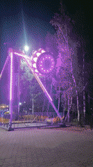 Illuminated amusement park with rotating rides and decorative archways observed