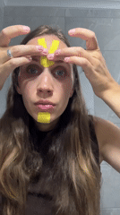 Woman applies kinesiology tape to face in Fethiye bathroom