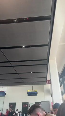 The video shows a departure board in an airport, displaying flight information for Ryanair flight FR 177 to London STN (Stansted). The flight is scheduled to depart at 19:00, and the status reads "Boarding folgt," meaning "Boarding follows" in German, or "Boarding soon" in English. A message is displayed below, reminding passengers to have their passport and visa ready. The surrounding airport environment includes other people waiting, luggage, ceiling lights, a fire extinguisher, doors with restroom symbols and a soft drink vending machine.
