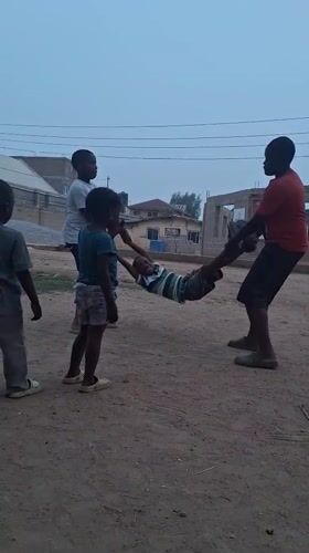 Children play swinging game on dirt road in Nigeria