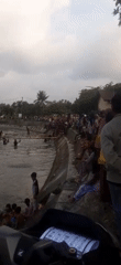 Locals gather at a canal in Sepakek, some balancing on logs