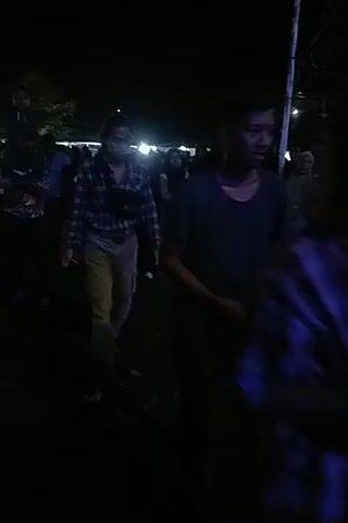 Here is a description of the video:

The video appears to be shot at night at an outdoor gathering.  The lighting is dim, but string lights are visible in the background, suggesting a celebratory or festive setting. Several people are present, though their features are not easily distinguishable due to the darkness. Some people appear to be dancing or moving to music, which can be heard in the background. The person recording the video is also moving, which makes the image appear unsteady and tilted at times.