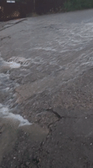 Fast-moving floodwater overtakes a cracked Sochi road in heavy rain.