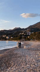 Couple walks dog on Adriatic beach during Montenegro sunset