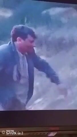 The video shows a man running in a hazy environment, carrying a white object. He stops and yells, appearing distressed, and continues to walk into the hazy background of trees and a light-colored sky. The recording is taken of a screen displaying the scene, with the watermark "TECNO SPARK Go 2" visible in the bottom left corner.