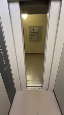 The video shows an upward view of an interior elevator. The elevator doors are closing. A control panel with several round buttons is visible. The floor appears to be covered in a beige carpet. The doors are white.