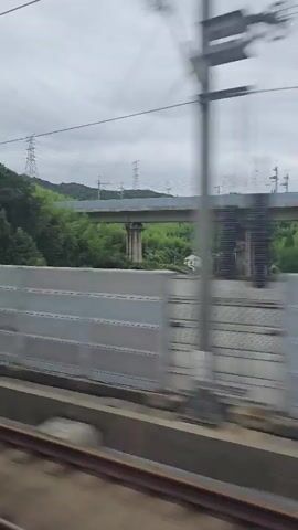 This video shows a view from a moving train. The first frame shows a view of greenery and trees outside the train, with a concrete barrier in the foreground. The second frame shows a dark interior of the train, with a light beam across the scene.