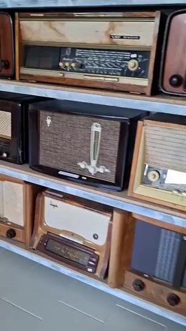 The video pans across shelves filled with vintage radios. The radios are of various sizes and designs, with wooden casings, fabric speaker grilles, and knobs. The shelves appear to be made of metal. The environment seems to be a display or collection room. There are no people visible in the video.