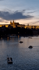 Prague Castle glows at dusk over a boat-dotted Vltava