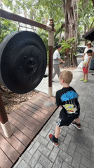 Striking a large gong at an outdoor site in Ko Samui