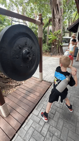 Striking a large gong at an outdoor site in Ko Samui