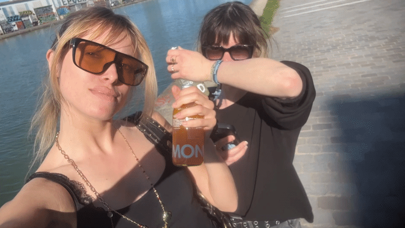 Two women share drinks by canal in Pantin
