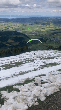 Paraglider spotted descending over Swiss mountain landscape near Schwende-Rüte