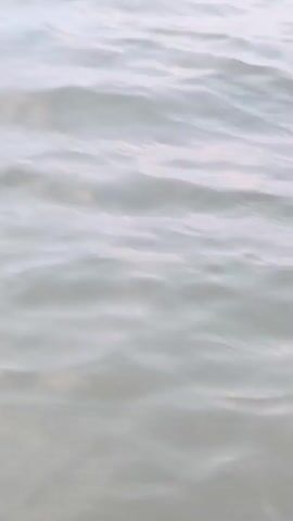 This media file captures a serene scene of a body of water, likely the Caspian Sea given the location context of Balaca Həmyə, Azerbaijan. The footage begins with a close-up of gently rippling water, suggesting a calm day. As the camera pans out, the vast expanse of the sea meets a muted, overcast sky, indicating possibly a cloudy or dusk setting.

In the latter part of the video, two individuals are visible in the water. One person, wearing a pink bikini, is seated on a floating object, possibly a boogie board, while another person appears to be in the water nearby. Their figures are somewhat indistinct due to the distance and the lighting conditions. The activity suggests recreational use of the water, such as swimming or playing.

There are no discernible signs or text within the video. The overall mood is tranquil and peaceful, with the overcast sky contributing to a soft, diffused light. The location cues point to a coastal area in Azerbaijan, likely a beach or bay. The activity is casual and appears to be a moment of leisure.