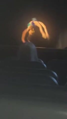 The video shows a gymnast performing a handstand on a raised platform. The gymnast is wearing a blue and green leotard. The background is dark, with some blurry lights and structures visible. The gymnast's body is in a clear arched position, with legs extended upwards and hands placed on the platform. The overall scene appears to be a performance or competition, possibly indoors given the lighting conditions. The camera angle is low, looking up at the gymnast. The video is short, lasting only a few seconds, and there is no visible text. The atmosphere appears energetic and focused on the gymnastic feat.