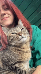 Woman with red hair pets tabby cat while smiling