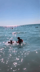 Crowded beach day with kids playing in turquoise surf