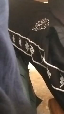 The video shows a close-up of black pants with white stripes and the Kappa logo. The pants appear to be made of a smooth material and are likely athletic wear. The stripes run along the side of the leg and are decorated with repeating Kappa logos. The background is blurred but appears to be an indoor setting with some wooden furniture.