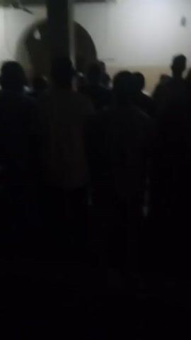 The video shows a blurry, dark scene with silhouettes of people. The lighting is dim, making it difficult to discern details. It appears to be indoors or at night. There is a sense of a crowd or gathering, but the lack of clarity prevents any specific identification of individuals or activities. The camera seems to be held by someone within the group, possibly recording a performance or an event. The overall impression is one of a low-light, possibly crowded, situation.