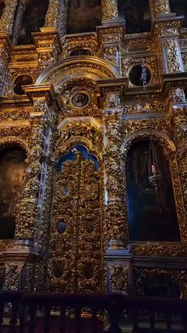 The video shows a highly ornate golden door in what appears to be a church or cathedral. The door is covered in intricate carvings and details, with small oval portraits set into the door's surface. The background behind the door appears to be blue. The columns to the sides of the door are also intricately carved and gold-colored. The camera slowly zooms in to show the door in greater detail.