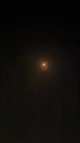 A brief video shows a cluster of lights in the dark sky. The lights start out with a reddish-orange hue, and then morph into a mix of yellow, green, and red lights. The lights remain suspended in the night sky throughout the video. The setting appears to be outdoors during nighttime, with no other visible objects or people.