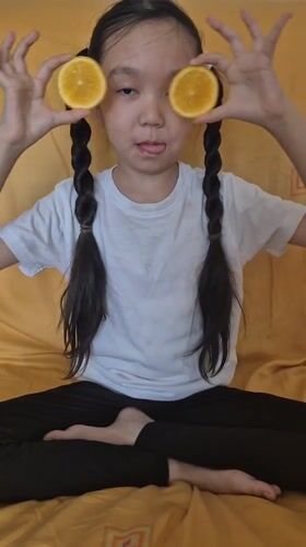 Girl enjoys orange snack on bed in Kokshetau