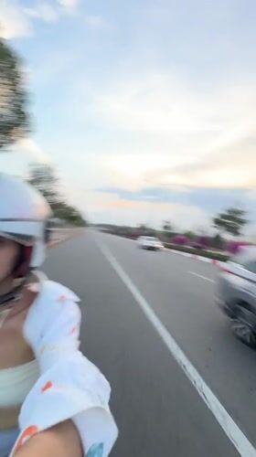 Woman rides scooter through Mui Ne wearing white helmet