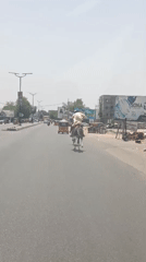 Two horsemen ride through Nigerian town street carrying sack
