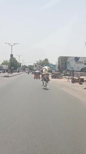 Two horsemen ride through Nigerian town street carrying sack