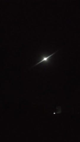 This media file depicts a nighttime scene, likely outdoors, with minimal ambient light. The primary visual element is a bright, solitary light source positioned slightly left of center in the frame. This light source is a small, intense white point, from which a noticeable lens flare extends diagonally upwards and to the left. The rest of the image is predominantly dark, suggesting a deep night sky or an unlit environment.

In the upper right corner of the frame, there is a faint, rectangular shape that appears to be illuminated from within or reflecting light. It is indistinct and somewhat blurred, making its precise nature difficult to ascertain, but it hints at a structure or object with some form of lighting.

The overall atmosphere is one of darkness and quietude. There are no visible people, animals, or prominent natural features like trees or buildings, beyond the potential structure in the upper right. The scene appears still and unmoving. The time of day is clearly night, with the darkness and the presence of artificial or celestial light sources being the only indicators. The weather is not discernible from the image. No specific location cues are immediately apparent, other than the provided context of Khalkabad, Uzbekistan, which would imply the setting is within or near that area. The absence of any identifiable subjects or activities evokes a sense of solitude or observation of a distant, illuminated point. There is no visible text in the media file.