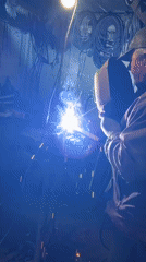Man welding in cluttered workshop with safety gear