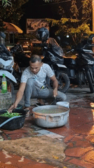 Man washes vegetables on pavement in Lhokseumawe evening