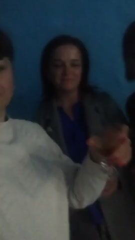 The blurry, low-light video captures three women posing together in an indoor setting against a solid, textured blue wall in Sîngera, Moldova.

In the foreground, slightly to the left, a woman with short dark hair, wearing a light-colored top, looks towards the camera with a slight smile. Her hand, adorned with red nail polish, holds a clear glass containing an amber liquid.

Behind her, in the middle, another woman with dark hair wears a blue top under a dark jacket. She also holds a similar glass and smiles faintly.

To the right and slightly further back, the third woman, wearing a dark turtleneck and dark hair, holds a glass and offers a subtle smile.

The overall impression is of a casual social gathering or celebration. The dim lighting and the blur suggest either movement during capture or challenging lighting conditions. All three women appear relaxed and content, holding their drinks as if toasting or enjoying the moment.

Accompanying the video is a cheerful and upbeat instrumental music track, featuring what sounds like a plucked string instrument (possibly a ukulele or acoustic guitar), contributing to the lighthearted mood of the scene. No visible text is present in the video.